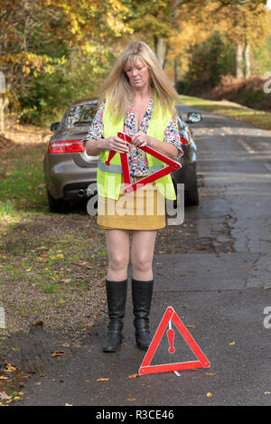 Driver donna mettendo una sicurezza riflettente di un triangolo di avvertimento sul lato posteriore di una macchina Foto Stock