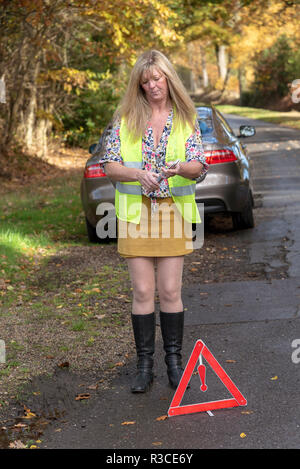 Driver donna mettendo una sicurezza riflettente di un triangolo di avvertimento sul lato posteriore di una macchina Foto Stock