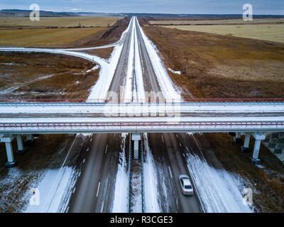 Antenna; drone vista di autostrada in campagna; strade vuote con la neve sulle banchine stradali; del terreno di campagna con Giallo autunno i campi e i primi fiocchi di neve; Foto Stock