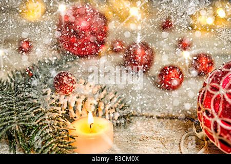 Rosso albero di natale sfera con candela e fir ramo su un vecchio tavolo di legno con la neve Foto Stock