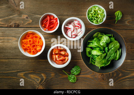 Verdure fresche e verdi su cucina piano di lavoro in legno, vista dall'alto. Ingredienti per insalata - Spinaci, carote cetrioli e pomodori e ravanelli. Mangiare sano Foto Stock