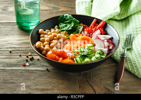 Buddha colorato ciotola con ceci, carote, pomodori, cetrioli, radicchio e peperoni su di un tavolo di legno. Insalata vegetariana. Foto Stock