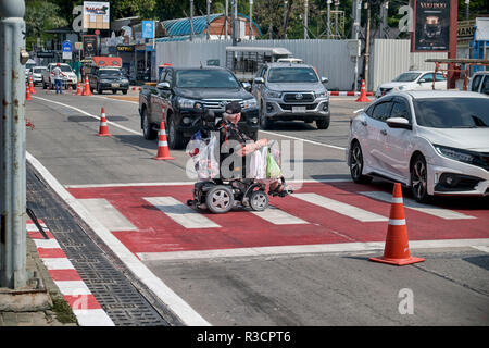 Persone disabili su carrozzina uomo in una sedia elettrica che attraversa la strada sulle strisce pedonali. Thailandia del sud-est asiatico Foto Stock