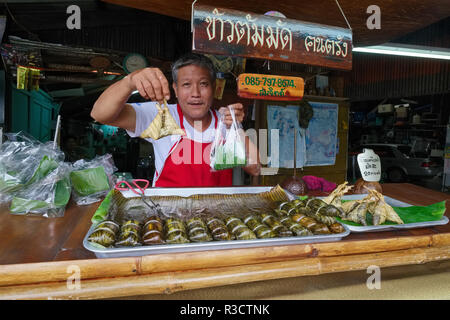 Un venditore nella città di Phuket, in Thailandia, con alcuni dei suoi tradizionali dessert o dolci tailandesi, come Khao Thom Mad (Mat), avvolto in foglie di pandano Foto Stock