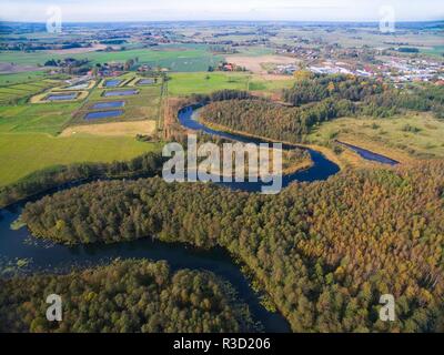 Meandro del fiume Wegorapa che scorre attraverso le zone umide durante la stagione autunnale, Wegorzewo città in background, Mazury, Polonia Foto Stock
