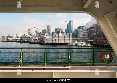 Stati Uniti d'America, WA, Seattle. Lungomare nel sole di mattina incorniciato dalla struttura del traghetto. Seattle grande ruota e lo Space Needle Foto Stock