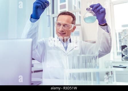 Interessante la chimica. Lieta operatore sanitario mantenendo il sorriso sul suo viso mentre i reagenti a confronto Foto Stock