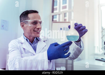 Essere positivo. Bel giovane mantenendo il sorriso sul suo viso durante il lavoro in laboratorio Foto Stock