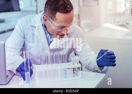 La ricerca scientifica. Allegro lavoratore medico mantenendo il sorriso sul suo viso durante il lavoro in laboratorio Foto Stock