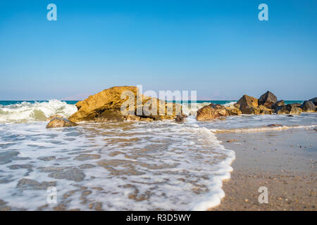 Paesaggio greco raffigurante le onde tranquille e schiuma di mare intorno a una formazione delle rocce sulla terra. Foto Stock