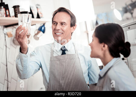 Assolutamente pulito. Positivo uomo bello guardando il vetro mentre si verifica la sua pulizia Foto Stock