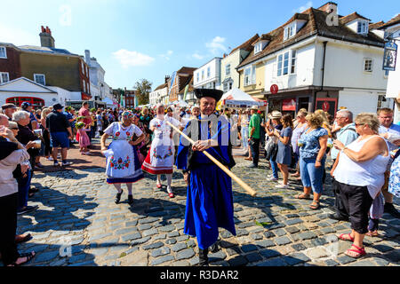 Faversham hop festival, parata. Balaton ballerini ungherese, piombo da uomo in manto azzurro, marciando attraverso la strada affollata con gli spettatori a guardare. Foto Stock