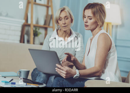 Consultazione. Giovane professionista consulente finanziario seduto vicino a gravi di età compresa tra donna e discutere questioni di lavoro mentre puntare il dito sullo schermo del notebook Foto Stock