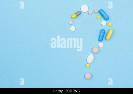 Varie pillole e capsule a forma di punto interrogativo segno su sfondo blu con una copia dello spazio. Vista superiore Foto Stock