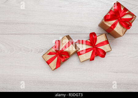 Tre confezioni regalo legati con nastri di colore rosso e grigio Sfondo di legno. Concetto di regali. Vista da sopra con copia spazio. Foto Stock