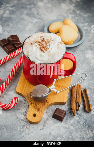 Natale smaltato rosso con tazza di cioccolata calda e panna montata, bastoncini di cannella, anice stelle e abbondante zucchero frollini cookies e candy canes su Foto Stock