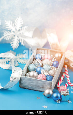 Rosa, argento e blu le palle di Natale, argento perle di Natale in una scatola di legno e canne di caramella su uno sfondo blu Foto Stock