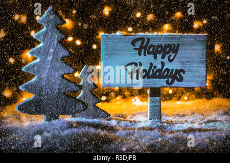 Rustico cartello in legno con la calligrafia Inglese Buone Vacanze. Albero di Natale sulla neve e le luci fairy in background. Spotlight blu Foto Stock