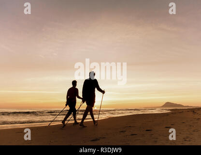 Coppia matura passeggiate con racchette Nordic walking, sulla spiaggia al tramonto in Spagna. Foto Stock