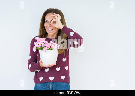 Medio Evo Woman holding fiori pot impianto isolato su sfondo con buon viso sorridente facendo segno OK con la mano sull'occhio guardando attraverso le dita Foto Stock