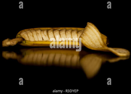 Una banana tagliata ancora nella sua buccia con un riflesso su uno sfondo nero Foto Stock