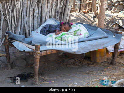 Ragazza etiope in appoggio su un letto di fronte alla sua casa, regione di Afar, Assayta, Etiopia Foto Stock