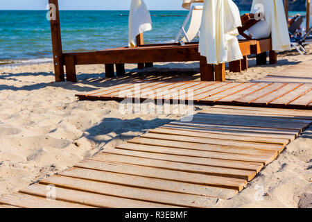 Percorso di legno sta andando attraverso la spiaggia sabbiosa, alla comoda pergola in legno con tenda bianca sunny beach. Foto Stock