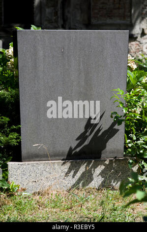 Austero lapide in un cimitero di Berlino in Germania con la luminosa luce del sole e ombre di un impianto sulla pietra e nessun nome inciso Foto Stock