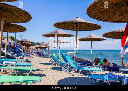 Vista sul pubblico vuoto spiaggia con ombrelloni di paglia, ombrelloni e sedie a sdraio per una vacanza perfetta. Foto Stock