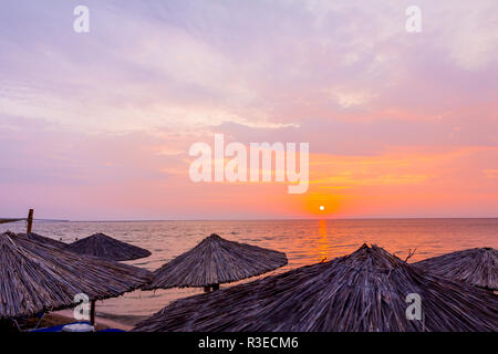 Vista sopra alla mattina presto Sun, dawn, sulla spiaggia pubblica con ombrelloni di paglia, ombrelloni collocati lungo il mare, le coste. Foto Stock