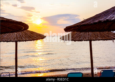 Vista in mattina presto Sun, dawn, sulla spiaggia pubblica con ombrelloni di paglia, ombrelloni e sedie a sdraio lungo la costa del mare. Foto Stock