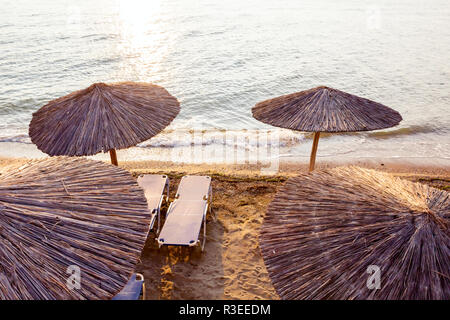 Vista sopra alla mattina presto Sun, dawn, sulla spiaggia pubblica con ombrelloni di paglia, ombrelloni e sedie a sdraio lungo la costa del mare. Foto Stock