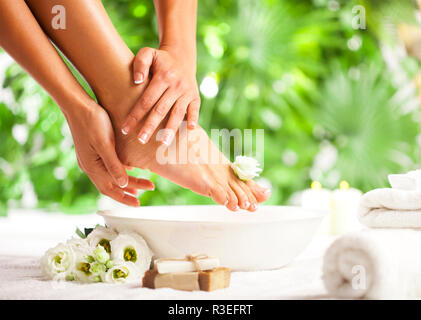 Femmina di mani e piedi con spa ciotola, asciugamani, sapone e fiori sul pavimento bianco e verde tropicale lascia lo sfondo Foto Stock