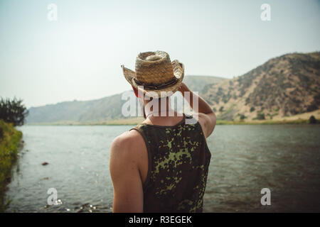 Foto candida di un uomo in cappello da cowboy che guarda il fiume e gode della vista. Faccia in non visibile. Foto Stock