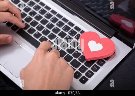 Persona della mano la digitazione sulla tastiera del notebook con cuore rosso Foto Stock