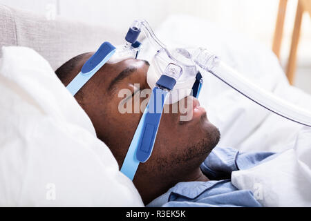 Elevato angolo di visione di un giovane africano indossando maschera CPAP dormire sul letto Foto Stock