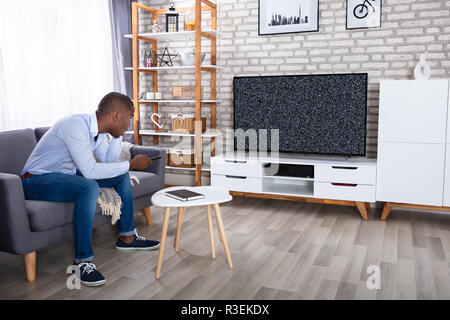 African uomo seduto sul letto guardando la televisione con Nessun segnale Foto Stock