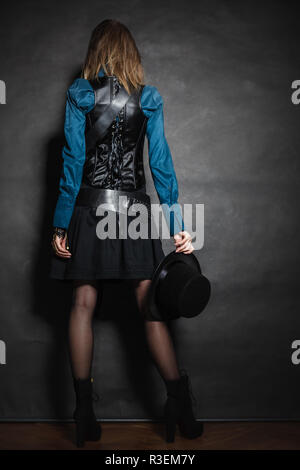 A piena lunghezza steampunk donna retrò con cilindro di vista posteriore studio shot grunge sfondo scuro Foto Stock