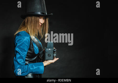 Fotografia e stile retrò. Vintage giovane ragazza attraente detiene il vecchio di età compresa la fotocamera. Steampunk fotografo di prendere foto. Foto Stock