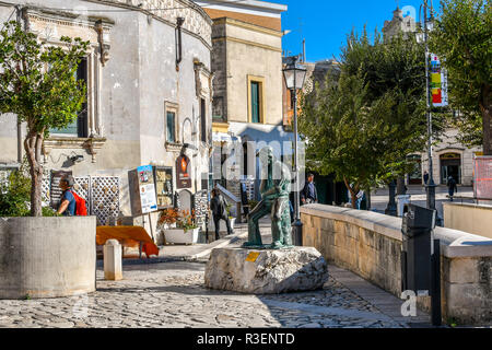 Le persone passano in negozi di souvenir vicino alla statua di bronzo di un uomo di pensiero nella Piazza Vittorio Veneto di Matera, Italia, nella regione Basilicata Foto Stock