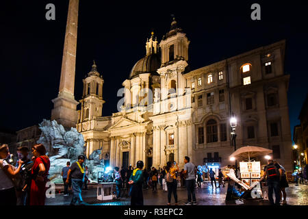 Il turista a godere gli artisti e i venditori in strada a fianco dei Quattro Fiumi la fontana della piazza Navona sotto le luci della chiesa di Sant'Agnese Foto Stock