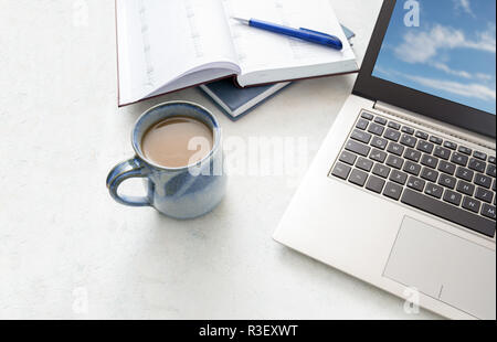 Laptop, calendario e un blu tazza di caffè su un tavolo luminoso, copia dello spazio, messa a fuoco selezionata Foto Stock