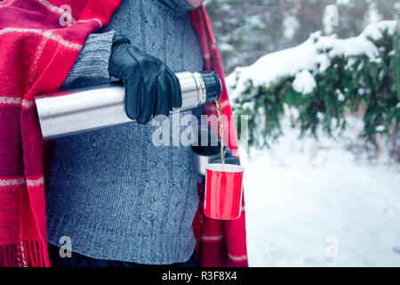 L'uomo versa il tè caldo fuori dei thermos in inverno forest Foto Stock