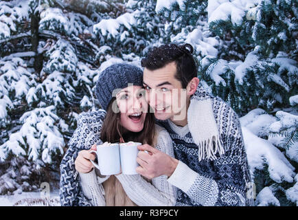 Giovane abbracci e beve caffè con marshmallow nella foresta di inverno Foto Stock