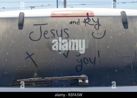 "Gesù vi ama' scritto nella sporca parabrezza posteriore di un veicolo parcheggiato iin downtown San Diego, California, Stati Uniti. Foto Stock