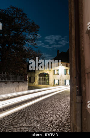 Striature di vetture passando attraverso una stretta strada del villaggio con vecchie case sotto una luna piena sky in background Foto Stock