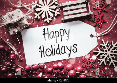 Etichetta con la calligrafia Inglese Buone Vacanze. Piatto con laici rustico rosso decorazione di Natale come dono, slitta e fiocchi di neve Foto Stock