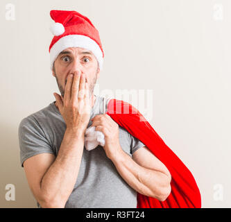 Senior uomo che indossa il natale di santa claus hat coprono la bocca con la mano sconvolto con vergogna per errore, espressione di paura, paura in silenzio, segreto conce Foto Stock