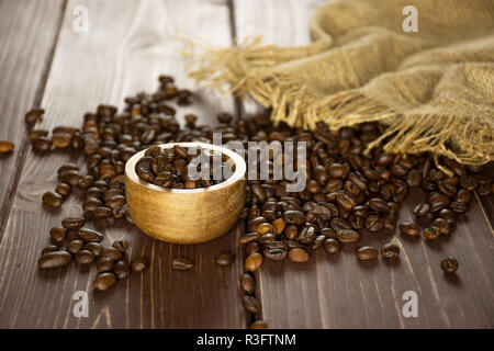Sacco di tutta marrone scuro i chicchi di caffè arabica dolce varietà sacco di iuta con ciotola di legno su legno marrone Foto Stock