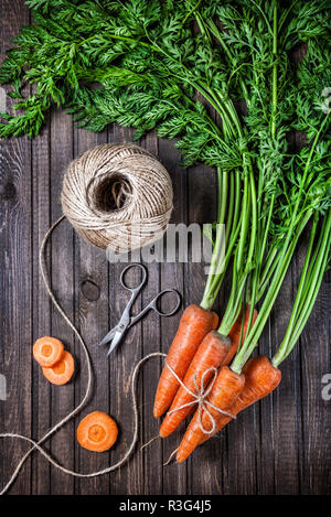 Materie carota con foglie verdi, forbici e fune su sfondo di legno Foto Stock